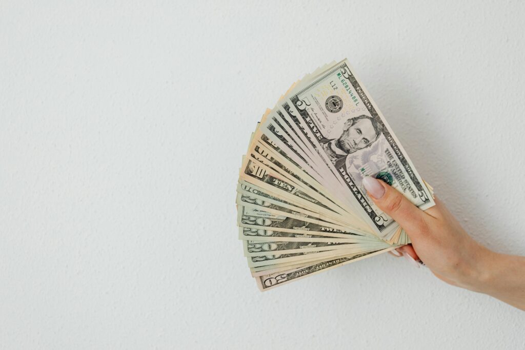 A hand holding an array of US dollar bills, fanned out against a plain white background.