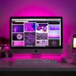 Modern desk setup with neon lighting and a desktop computer displaying colorful images.