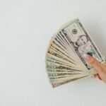 A hand holding an array of US dollar bills, fanned out against a plain white background.